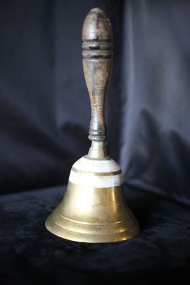 une cloche en laiton munie d'une poignée en bois, sur fond noir