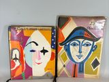 two paintings of faces are displayed on a shelf next to each other