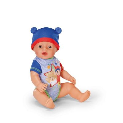 une poupée avec un bonnet bleu et un bavoir, assise par terre