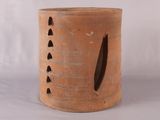 un grand vase marron percé de trous, posé sur une surface blanche