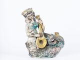 figurine d'un homme jouant d'un instrument de musique assis sur un rocher