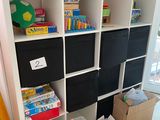 une bibliothèque blanche sur laquelle sont posés des bacs noirs et des jouets