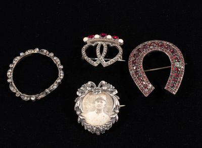 three silver brooches with red and white stones on a black background