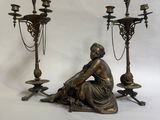 une statue représentant une femme assise par terre à côté de trois chandeliers