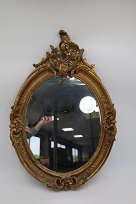 Miroir de forme ovale dans un cadre en bois et stuc doré à d…
