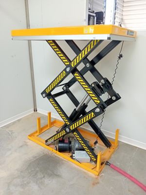 yellow scissor lift table in a garage with a red hose