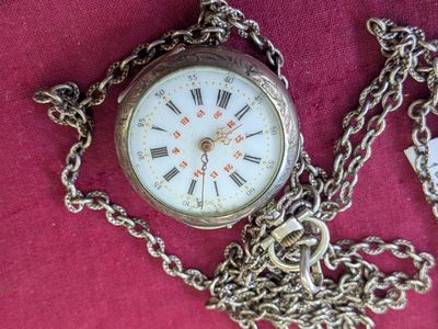 une montre de poche attachée à une chaîne, posée sur un tissu rouge