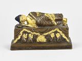 statue en bronze représentant une personne allongée sur un lit orné d'une décoration dorée