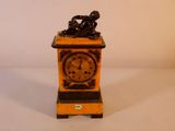 une petite horloge surmontée d'une statuette représentant un homme assis