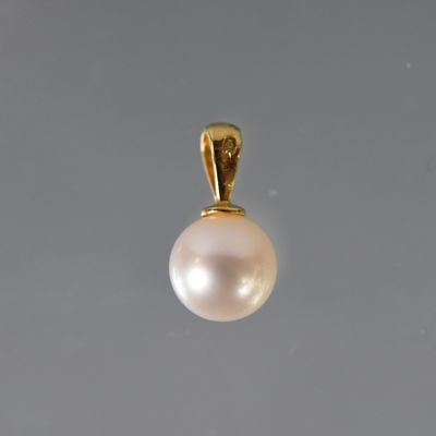 un pendentif en perle blanche est suspendu à une chaîne en or sur un fond gris