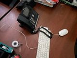a desk with a keyboard, mouse, phone, and other items on it