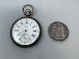 une petite montre de poche en argent à côté d'une pièce de dix cents