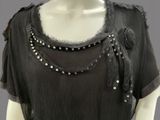 an image of a mannequin wearing a black top with silver beads and fringes