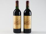 two bottles of red wine sitting next to each other on a white surface