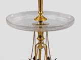 une table en verre avec un piètement doré et deux oiseaux posés dessus