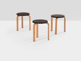 three wooden stools with black leather seats on a white surface