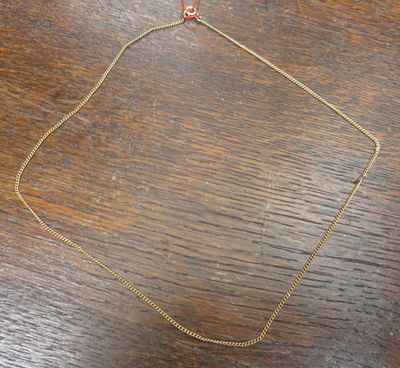 un collier à chaîne en or orné d'une perle rouge posé sur une table en bois