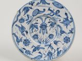 blue and white plate with birds and flowers on it on a stand