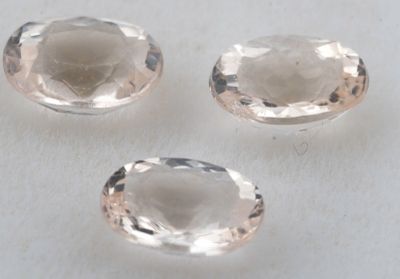 trois pierres précieuses de topaze blanche taillées en ovale, posées sur une surface blanche