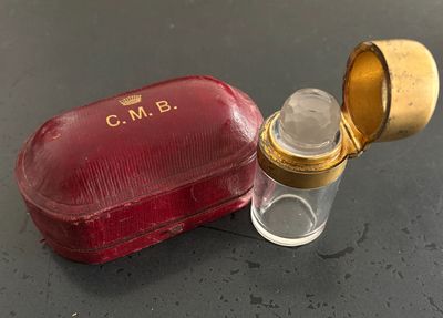 un petit étui rouge avec un couvercle doré, à côté d'un petit flacon en verre