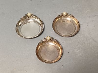 three silver plate coasters with pearls on them on a table