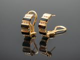 pair of black and gold earrings with diamonds on a reflective surface