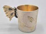a gold cup with a butterfly on the side of it
