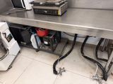 une grande table en inox dans une cuisine équipée d'un micro-ondes et d'un lave-vaisselle
