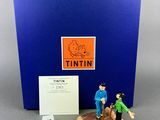 the figurine is sitting next to a blue box with a picture of a man and a dog on it