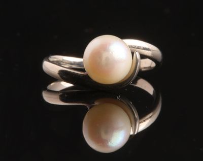un gros plan d'une bague en perle blanche posée sur une surface noire