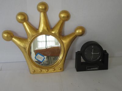 un miroir en forme de couronne dorée et une horloge posés sur une table