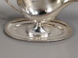 a silver gravy on a silver plate on a gray surface