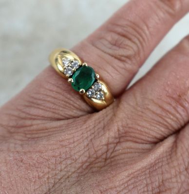 une image représentant la main d'une femme portant une bague en or sertie de trois émeraudes