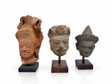 trois sculptures de têtes en pierre posées sur des socles en bois, sur fond blanc