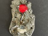 a close up of a metal object with a red stone on it