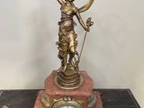 statue en laiton représentant une femme tenant une horloge posée sur une table en bois