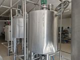 Des cuves en acier inoxydable sont alignées dans une usine, avec un ouvrier debout dessus