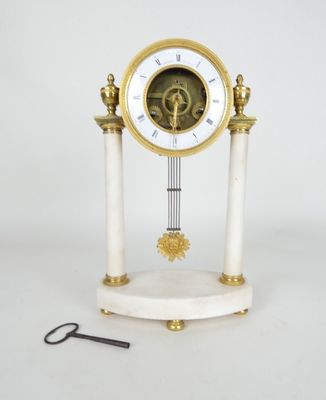 une horloge blanche et dorée posée sur un socle, avec une paire de ciseaux à côté