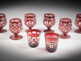six red glass goblets are lined up on a white surface