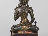 une statue en bronze représentant un Bouddha assis, posée sur un socle en bois