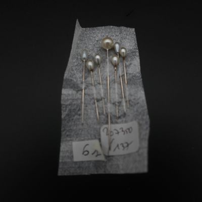 trois épingles en argent ornées de perles sont posées sur un morceau de papier