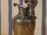 a silver vase sitting on a wooden table with a striped wall behind it