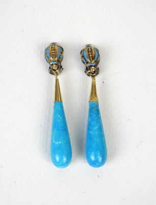 une paire de boucles d'oreilles turquoise et dorées posées sur un fond blanc