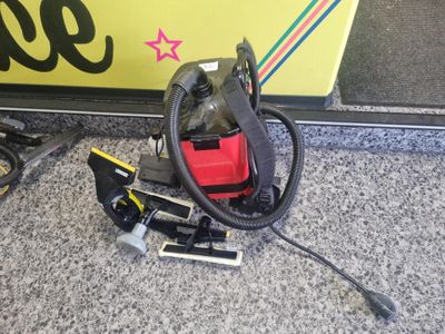 un aspirateur rouge et noir posé par terre à côté d'un panneau jaune et noir