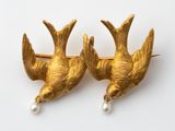 paire de broches en forme d'oiseaux en or, ornées de perles sur fond blanc