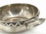 a silver bowl with a spoon in it on a white surface