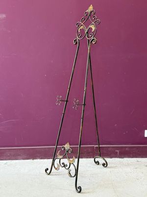 Un pupitre en fer forgé richement décoré se dresse devant un mur violet.