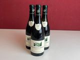 trois bouteilles de vin sont posées sur une table devant un mur rouge