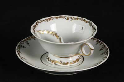a white cup and saucer with a gold decoration on it