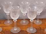six clear wine glasses are lined up on a wooden table